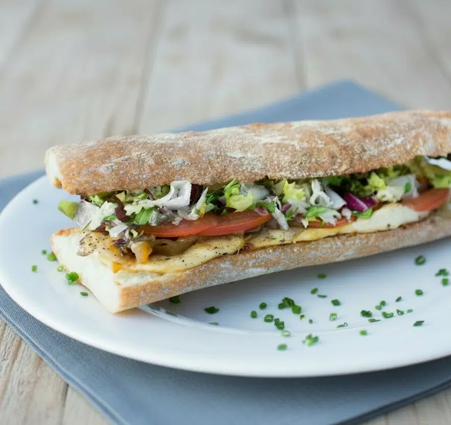 A filled baguette on a plate with garnish
